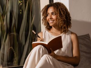 Femme noire souriante qui fait du journaling à sa fenêtre